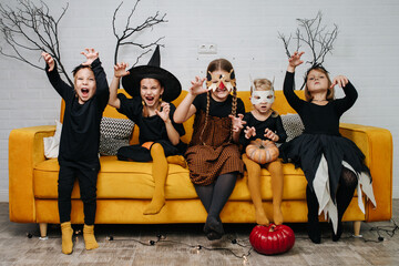 Little kids dressed for halloween party sitting on a couch, making tiger grimace