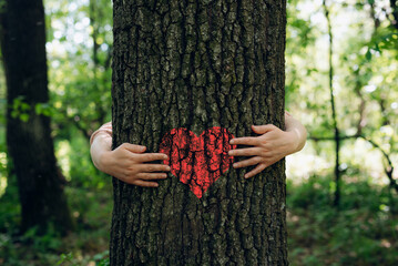 Family embracing the tree with red heart. Nature lover family.Concept of nature protection, care...