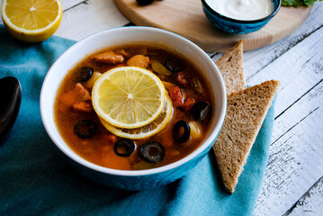 Salty soup with sour cream and lemon in a ceramic plate.