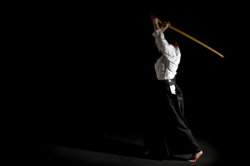 A girl in black hakama standing in fighting pose with wooden sword bokken over black background. Shallow depth of field.  - obrazy, fototapety, plakaty