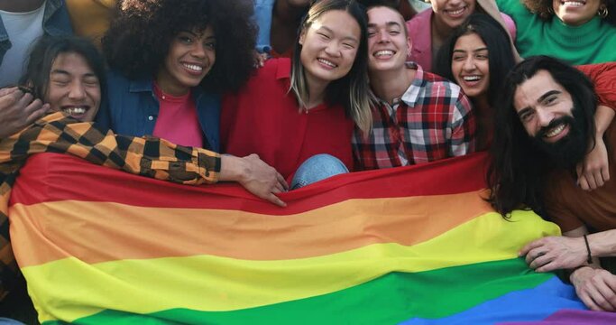 Diverse people having fun holding LGBT rainbow flag outdoor 