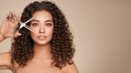 Beautiful young woman with a bright makeup and a afro  hair holds metal scissors. Model with curly...