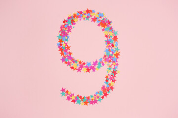 Number 9 or nine made from decorative multi-colored stars. Holiday numbers or figures. Top view