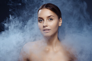 Portrait of beautiful young girl with clean, well kept skin isolated on dark background with smoke. Concept of beauty, art, ad, cosmetics