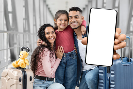 Travel App. Cheerful Middle Eastern Family At Airport Demonstrating Blank Smartphone