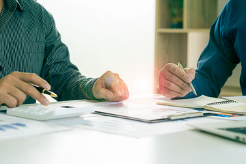 Close-up of two businessmen with pens pointing to graphs while chatting on wooden table with laptop, teamwork discussing up and down financial accounts, market economy.