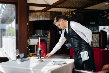 A young male waiter in a stylish uniform is engaged in serving the table in a beautiful gourmet restaurant. Restaurant activity, of the highest level.