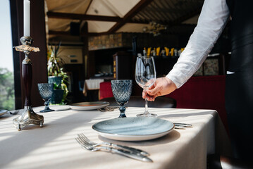 A young waiter in a stylish uniform is engaged in serving the table in a beautiful gourmet restaurant close-up. Restaurant activity, of the highest level.