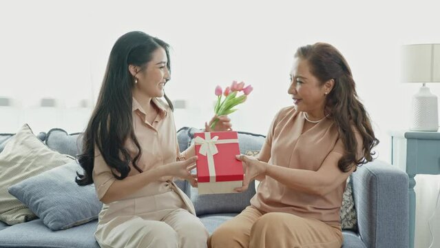 Attractive daughter asian give gift box and flower for mother in family moment celebrate mother day.