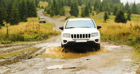 Fototapeta na wymiar white SUV, driving through a stupid puddle in the forest in the mountains. Front view, car travel in Carpathians, Ukraine, Europe
