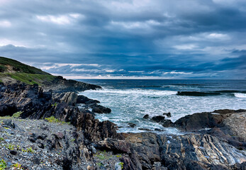 Fototapeta na wymiar Landscape view of an interesting complex rocky, coastal headland and a surf scene with dark, ominous storm clouds out to sea forming a background to this moody image.