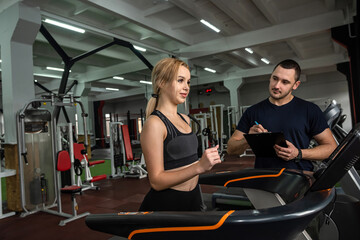 Fit female client running on treadmill with her personal trainer in a sport centre