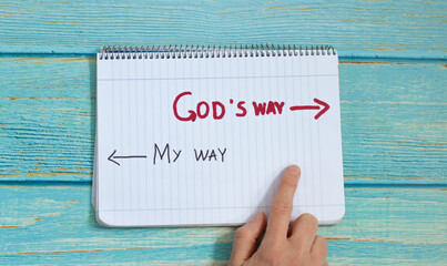 God's way, message quote on a notebook with a hand showing in direction to handwritten arrow isolated on a light blue wooden background. Top view. Follow Jesus Christ's path of eternal life concept. - obrazy, fototapety, plakaty