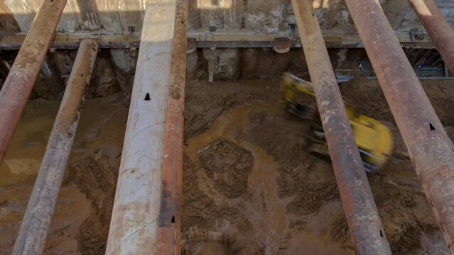 Excavators inside huge ditch pit at the construction site of the underground metro station line timelapse. Reinforcing structures from thick iron pipes of beams and structures.