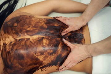 Obraz na płótnie Canvas female client lying and having cosmetician procedures with cacao chocolate treatment in spa