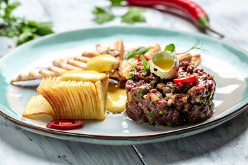French cuisine, beef steak tartare with raw quail egg yolk, capers, pickled cucumber with bread toasts served on plate. Restaurant menu, dieting, cookbook recipe top view