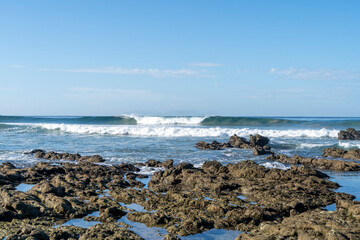 Fototapeta na wymiar Perfect wave over the rocks at beautiful beach Playa Hermosa. Surfing in Santa Teresa, Costa Rica.