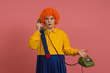 clown girl in a wig and a yellow-blue suit talking on a retro phone on a colored background