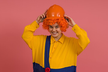 a cheerful clown in a wig and a yellow-blue suit puts a helmet on his head on a colored background