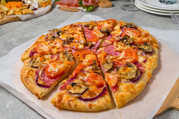 round pizza with sausage and mushrooms cut into pieces on the table