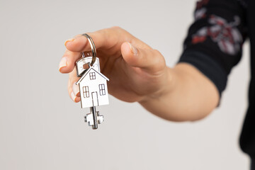 Woman hand giving a new metal key with home shaped keychain, isolated. New home concept