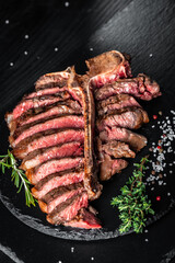 Piece of cooked T-bone or aged wagyu porterhouse grilled beef steak with spices served on on stone board. vertical image. place for text