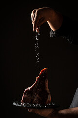 Chef hands cooking meat steak and adding seasoning in a freeze motion. Fresh raw Prime Black Angus...