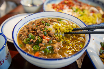 Saut�ed Pickled Beans with Minced Pork noodles f traditional Chinese Asian gourmet meal food dish on the brown wooden table, people eating with chopsticks.
