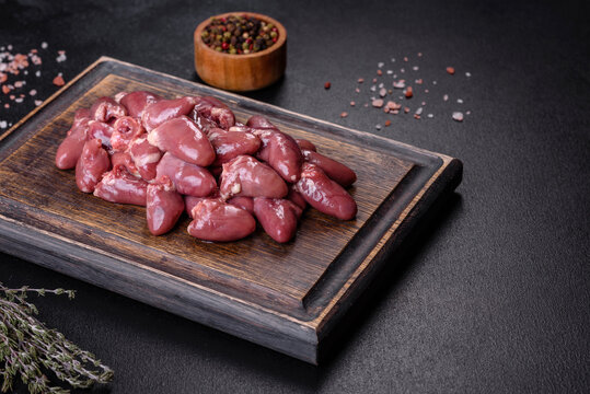 Raw uncooked chicken hearts on wooden cutting board on a dark concrete table