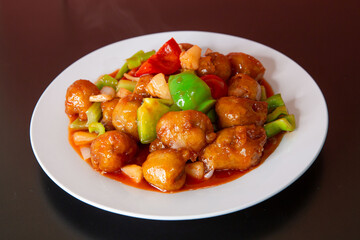 Sweet and sour pork of traditional Cantonese yum-cha Asian gourmet cuisine meal food dish on the white serving plate and brown red table