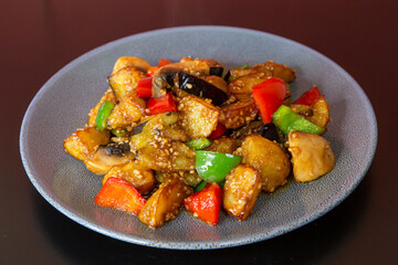 Stir-fried vegetables with eggplant, potato, capsicum of traditional Cantonese yum-cha Asian gourmet cuisine meal food dish on the white serving plate and brown red table