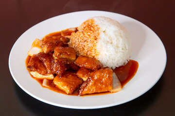 Sweet and sour fish on rice of traditional Cantonese yum-cha Asian gourmet cuisine meal food dish on the white serving plate and brown red table