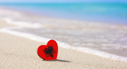 Flag of Albania in the shape of a heart on a sandy beach. The concept of the best vacation in Albania