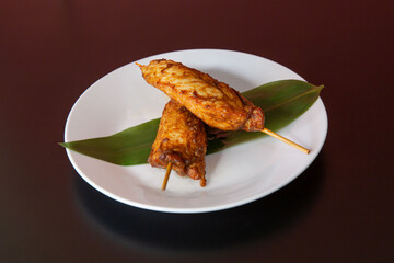 Roast fried chicken wing stick of traditional Cantonese yum-cha Asian gourmet cuisine meal food dish on the white serving plate and brown red table