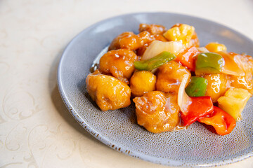 Sweet and sour pork with vegetables of traditional Cantonese yum-cha Asian gourmet cuisine meal food dish on the serving plate and white table