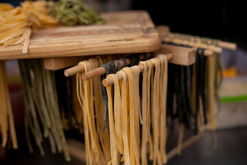 Egg noodles of different colors on a wooden board. Row of three small different colored bundles of...