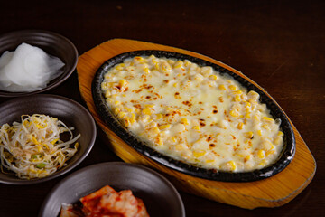Korean Grilled BBQ combo sets with Korean corn cheese on the wooden grilled plate and wooden table background, and pickle dishes