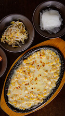 Top view of Korean Grilled BBQ combo sets with Korean corn cheese on the wooden grilled plate and wooden table background, and pickle dishes