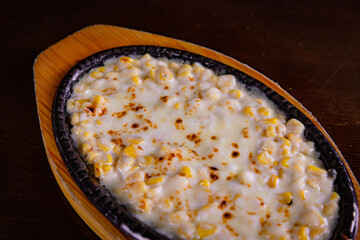Top view of Korean corn cheese on the wooden grilled plate and wooden table background