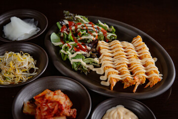 Korean Grilled BBQ combo sets with fried prawn and mayo with salad on the dark plate and black table vibe background, and pickle dishes