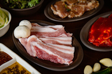 Korean Grilled BBQ combo with pork and marinated pork belly set on the traditional grill table, with lettuce, dipping sauce and pickle dishes