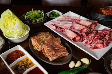 Korean Grilled BBQ combo with pork, wagyu, marinated beef set on the traditional grill table, with lettuce, dipping sauce and pickle dishes