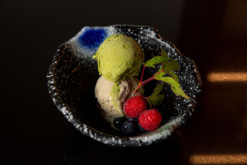 Matcha black sesame ice cream with berries in the kaiseki fine dining Japanese restaurant, with a fine black traditional bowl in black scene background