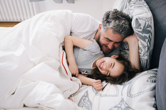 Cheerful daughter and father lying on bed at home