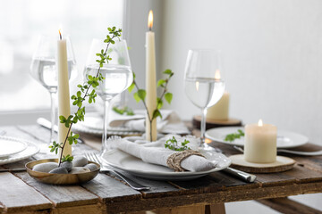 Rustic zero waste wedding decor with natural elements. Wooden table, candles, linen napkins, branches with green leaves. Eco-friendly decoration for the special dinner. Romantic and cozy place
