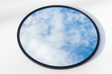 A round or oval mirror with a reflection of the blue sky and white clouds. Close-up. Isolated on a...