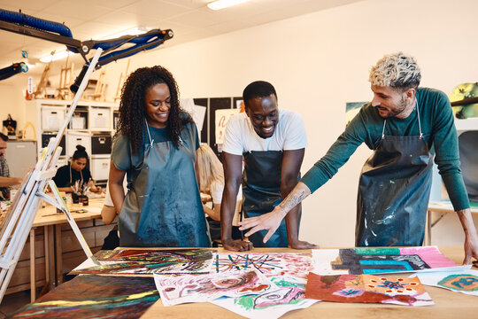 Young man discussing over paintings with friends standing at table in art class