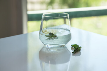 Refreshing drink based on lemon and mint. Tasty and healthy lemonade. A glass of lemonade sitting on a table with a window in the background.