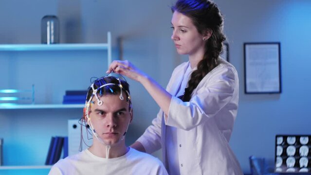 Man wearing EEG topographer for examining brain, doctor making electrogram of scalp activity. Researching of brain work using electroencephalography headset.
