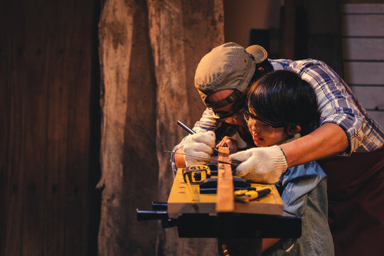 Asian carpenter in protective eyewear teaching son to practice learning and Concentrated to work with wood in his workshop, Success is a learnable skill, Practice learning for kids concept